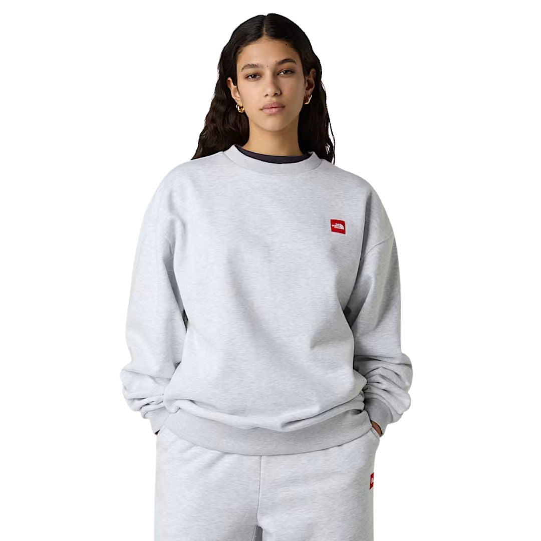 Sudadera The North Face Red Box Crew color Classic Grey Heather con logo rojo en el pecho, modelo mujer de frente.