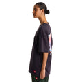 Camiseta The North Face Red Box oversize color obsidian, vista lateral sobre modelo con moño y pantalón verde, mostrando el perfil del estampado de espalda.