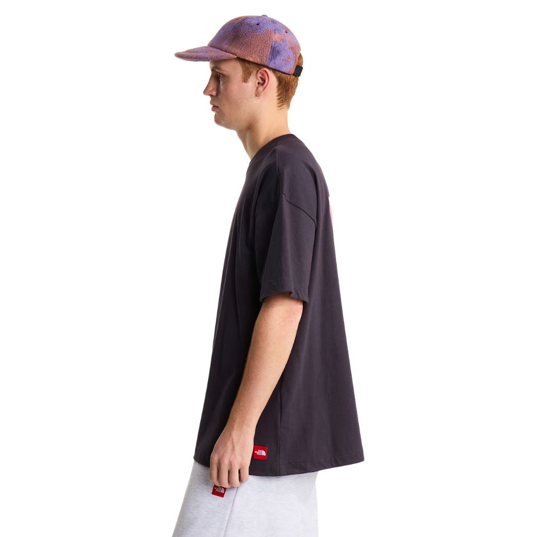 Camiseta The North Face Red Box oversize color obsidian, vista lateral de cuerpo entero sobre modelo con gorra, mostrando la manga corta ancha y la caída holgada.