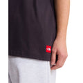 Camiseta The North Face Red Box oversize color obsidian, primer plano lateral del bajo con el parche bordado rojo THE NORTH FACE junto al brazo del modelo.