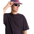Camiseta The North Face Red Box oversize color obsidian, primer plano frontal sobre modelo con gorra y gafas de sol tocando la visera, mostrando el cuello de canalé.