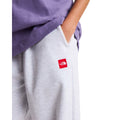 Detalle del bolsillo lateral del pantalón de chándal The North Face Red Box en gris jaspeado TFN Classic, con el parche rojo del logo bajo la costura.