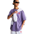 Look completo con pantalón de chándal The North Face Red Box en gris jaspeado TFN Classic, sujeto en la mano junto a camiseta oversize morada.