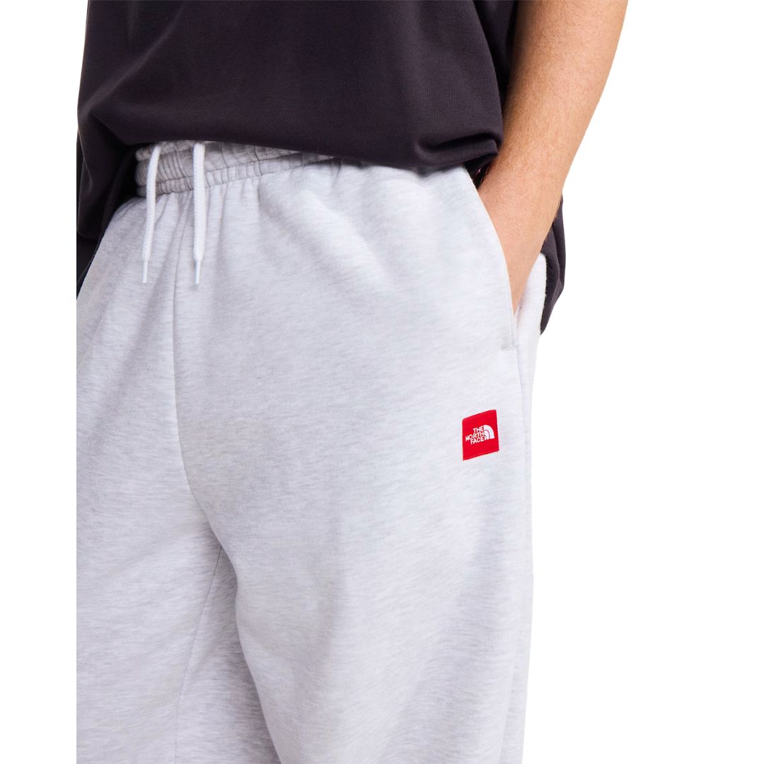 Detalle del pantalón de chándal The North Face Red Box en gris jaspeado TFN Classic: cintura elástica con cordón blanco y parche rojo del logo en la cadera.