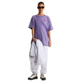 Look completo con pantalón de chándal The North Face Red Box en gris jaspeado TFN Classic, combinado con camiseta oversize morada y sudadera a juego sobre el brazo.