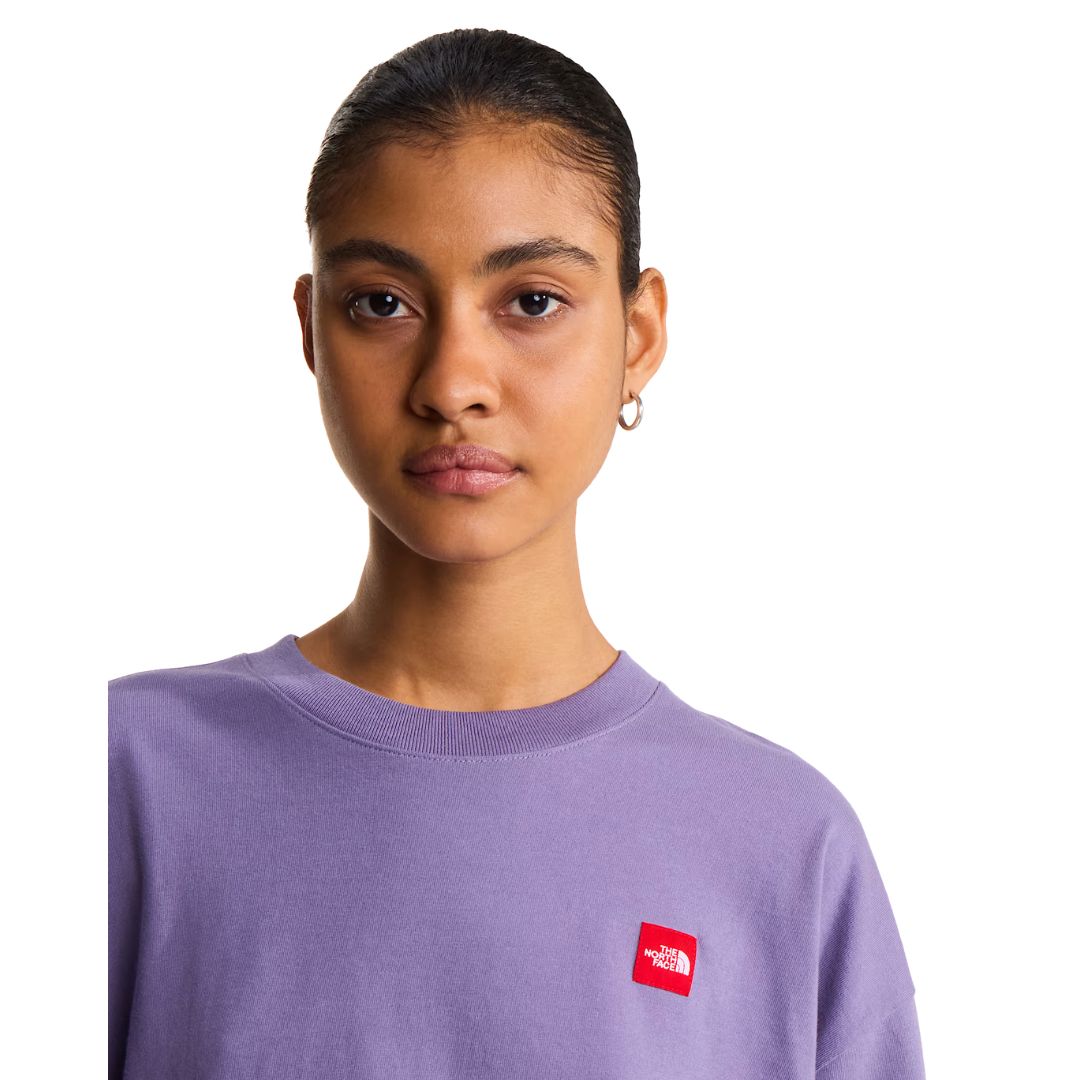 Detalle de cuello y parche de la camiseta The North Face Redbox unisex color Grounded Plum, primer plano del cuello de canalé y el logo bordado en rojo.
