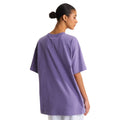Vista trasera de la camiseta The North Face Redbox unisex color Grounded Plum, mujer con moño alto mostrando el corte oversize y la caída holgada en la espalda.