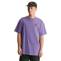Camiseta The North Face Redbox manga corta unisex color Grounded Plum, hombre con gorra verde mirando de lado, parche bordado rojo visible en el pecho.