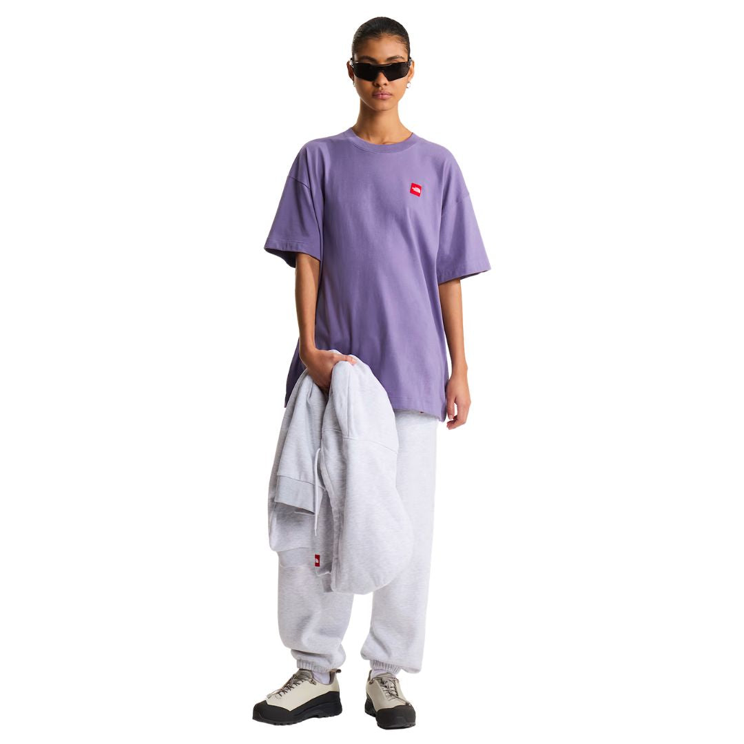 Camiseta The North Face Redbox unisex color Grounded Plum en look completo de cuerpo entero, mujer con gafas de sol, pantalón jogger gris y sudadera al hombro.
