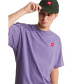 Camiseta The North Face Redbox manga corta unisex color Grounded Plum, hombre ajustándose una gorra verde, parche bordado rojo visible en el pecho izquierdo.