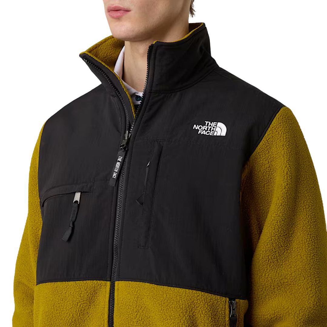 Primer plano del logotipo bordado en el pecho izquierdo de la chaqueta The North Face Retro Denali mostaza y negra