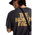 Detalle en primer plano del hombro y estampado trasero de la camiseta The North Face Stone Logo RLX en gris antracita, con bandolera cruzada sobre el gráfico 