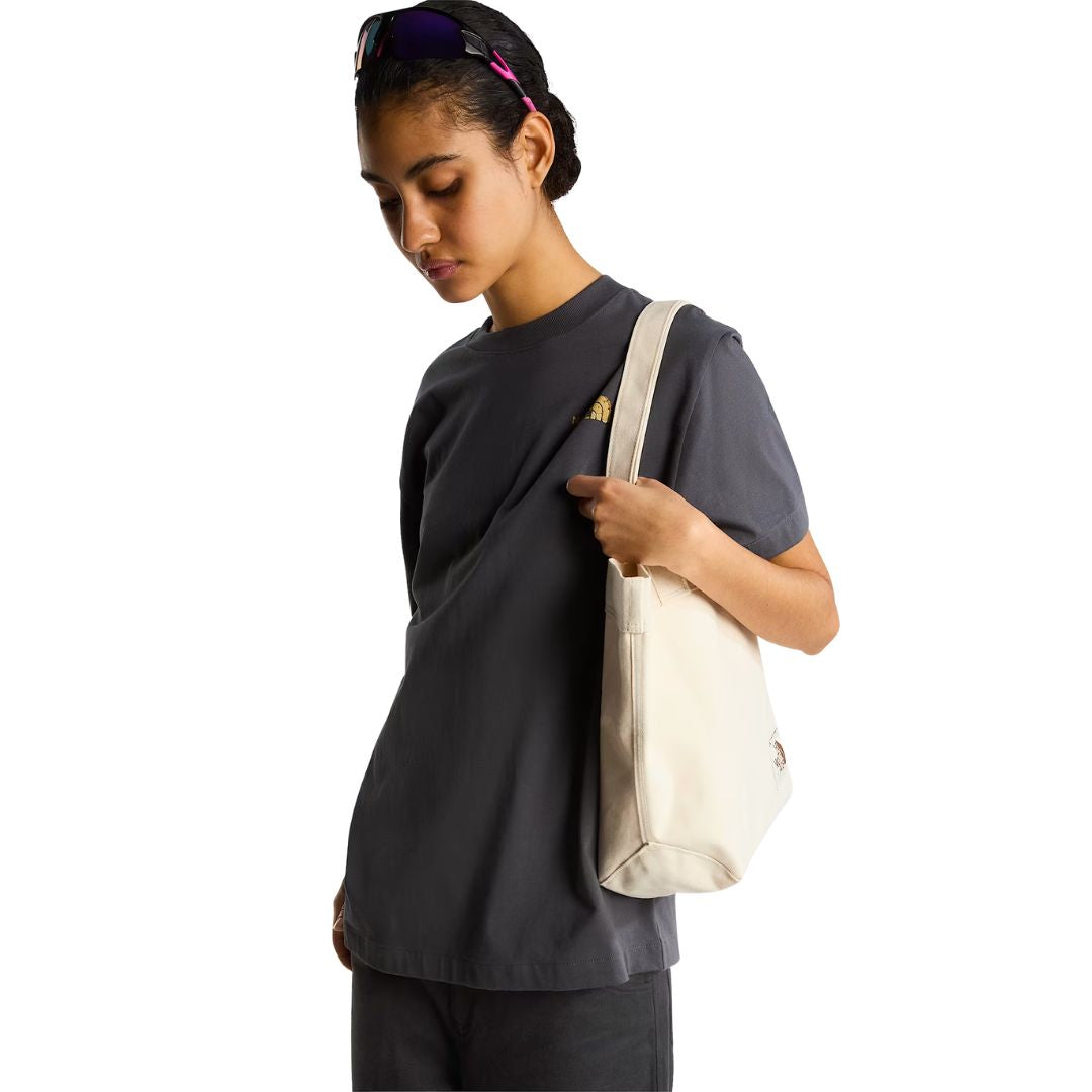 Camiseta The North Face Stone Logo RLX en gris antracita puesta en modelo mujer de perfil, con bolso tote a juego al hombro, mostrando la caída de la manga.