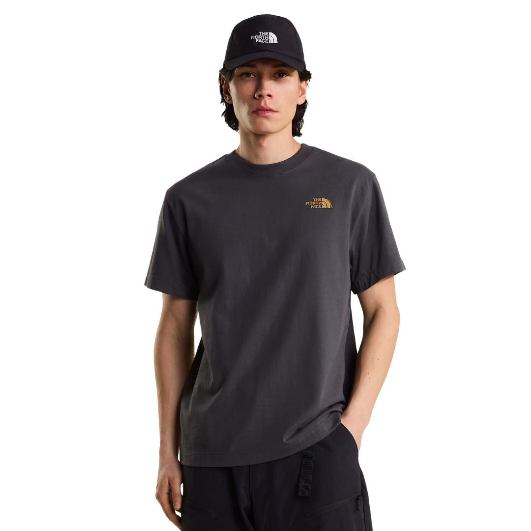 Camiseta The North Face Stone Logo RLX en gris antracita puesta en modelo hombre, vista frontal con gorra negra a juego, mostrando el logotipo pequeño en el pecho.