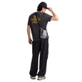 Camiseta The North Face Stone Logo RLX en gris antracita en modelo hombre de cuerpo entero por detrás, combinada con pantalón ancho negro y bandolera gris a juego, luciendo el estampado trasero.