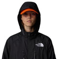 Mujer con la Chaqueta The North Face x Yinka Ilori Windshell Negra y gorra naranja y capucha puesta