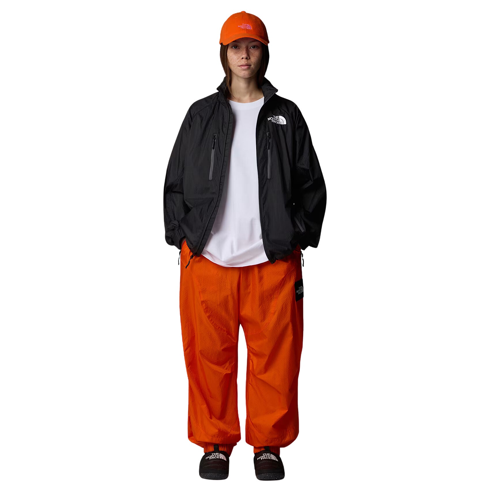 Mujer con la Chaqueta The North Face x Yinka Ilori Windshell Negra y gorra naranja vista completa