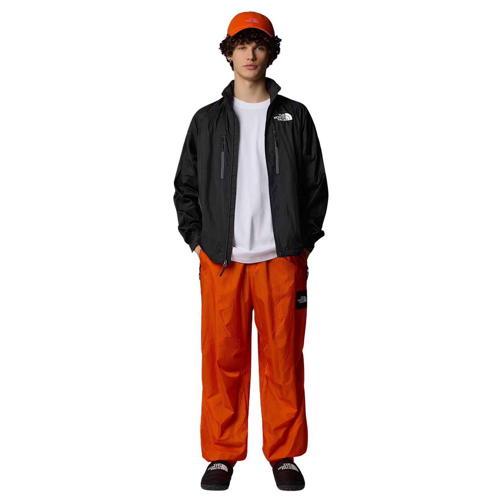 Hombre con la Chaqueta The North Face x Yinka Ilori Windshell Negra y gorra naranja vista completa