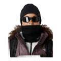 Modelo con gafas de sol y gorro oscuro lleva la braga The North Face Winter Seamless Reversible Neck Warmer TNF Black subida sobre la barbilla, con chaqueta con capucha de pelo