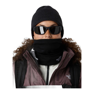 Modelo con gafas de sol y gorro oscuro lleva la braga The North Face Winter Seamless Reversible Neck Warmer TNF Black subida sobre la barbilla, con chaqueta con capucha de pelo