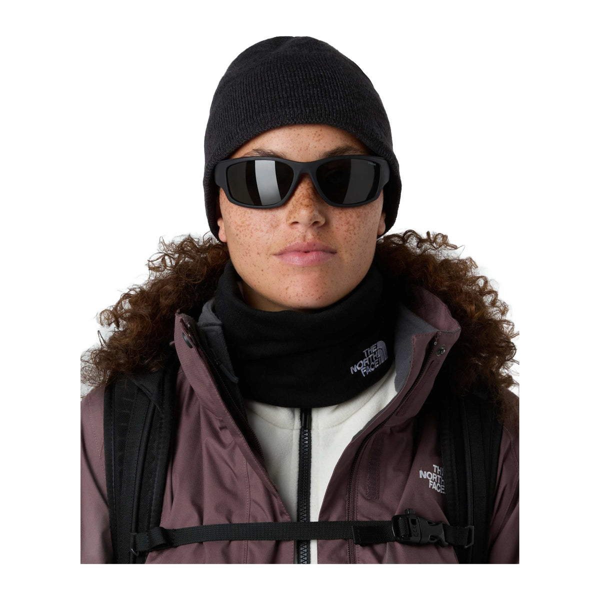 Modelo con gafas de sol y gorro oscuro lleva la braga The North Face Winter Seamless Reversible Neck Warmer TNF Black más baja alrededor del cuello, bajo una chaqueta con capucha de pelo