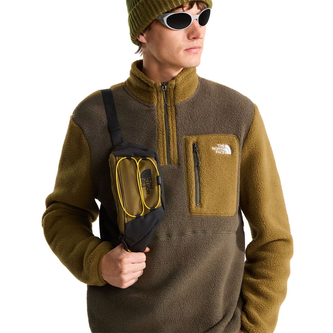 Modelo con la chaqueta polar The North Face Yumiori 1/4 Zip New Taupe Green/Caraway Seed y riñonera a juego, luciendo el bolsillo delantero con logotipo de la marca.