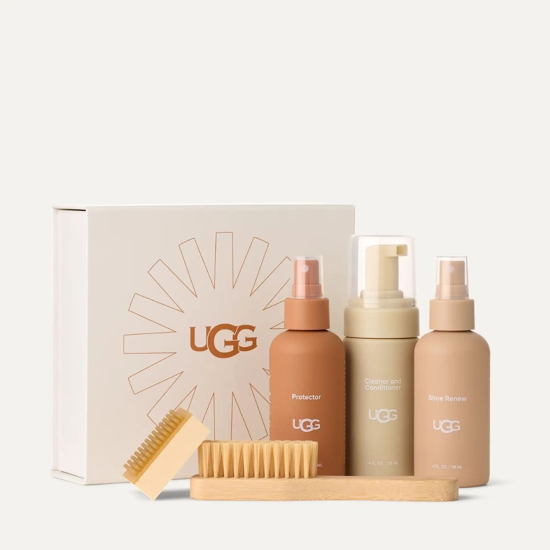 Caja del UGG Care Kit Cleaner con el logotipo UGG en forma de sol, junto a los tres botes del kit y el cepillo y eliminador de rozaduras colocados delante.