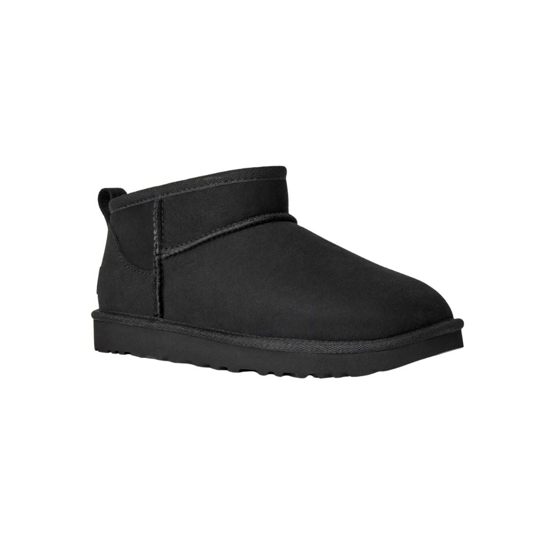 Vista en ángulo de tres cuartos de la bota UGG Classic Ultra Mini en color negro destacando la puntera redondeada, la trabilla trasera y la suela EVA antideslizante.