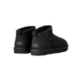 Par de botas UGG Classic Ultra Mini en color negro vistas desde atrás en ángulo, con la etiqueta UGG en el talón, la trabilla trasera y la suela flexible visible.