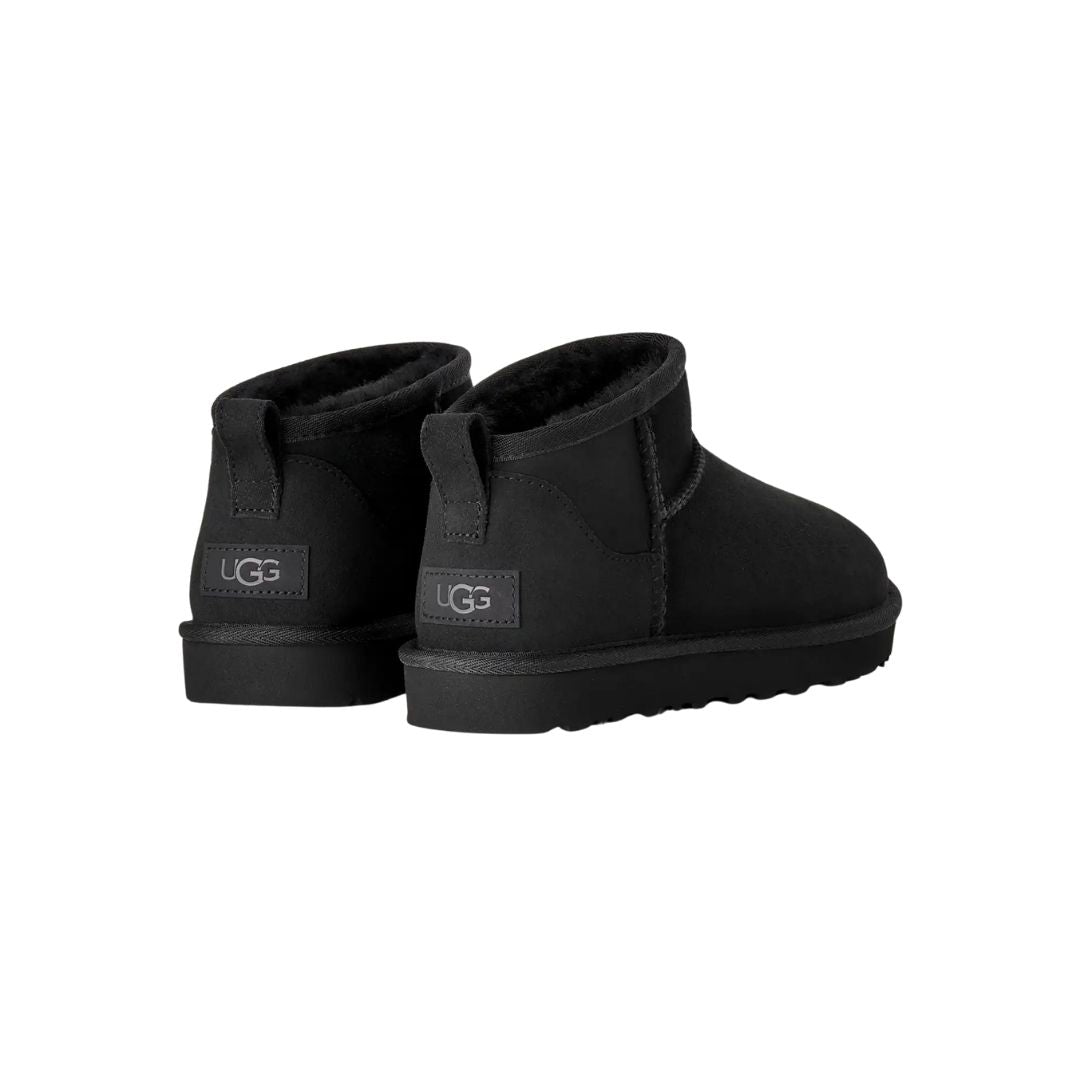 Par de botas UGG Classic Ultra Mini en color negro vistas desde atrás en ángulo, con la etiqueta UGG en el talón, la trabilla trasera y la suela flexible visible.