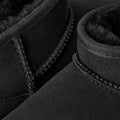 Primer plano de dos botas UGG Classic Ultra Mini en color negro mostrando las costuras decorativas sobrehiladas y el forro de piel de oveja en el borde superior.