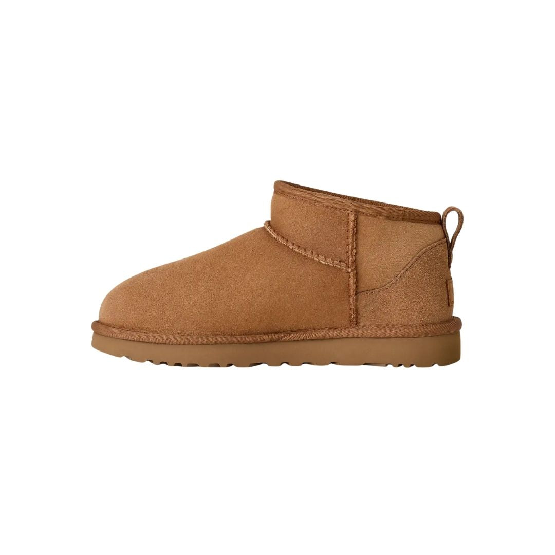 Vista lateral de la bota UGG Classic Ultra Mini en color chestnut mostrando la línea superior asimétrica, el pespunte central decorativo y la silueta de caña ultra corta.