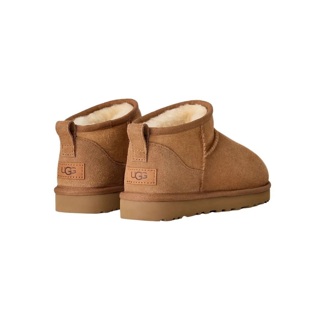 Par de botas UGG Classic Ultra Mini en color chestnut vistas desde atrás en ángulo, mostrando la trabilla trasera, el contrafuerte de ante y la suela flexible de goma.