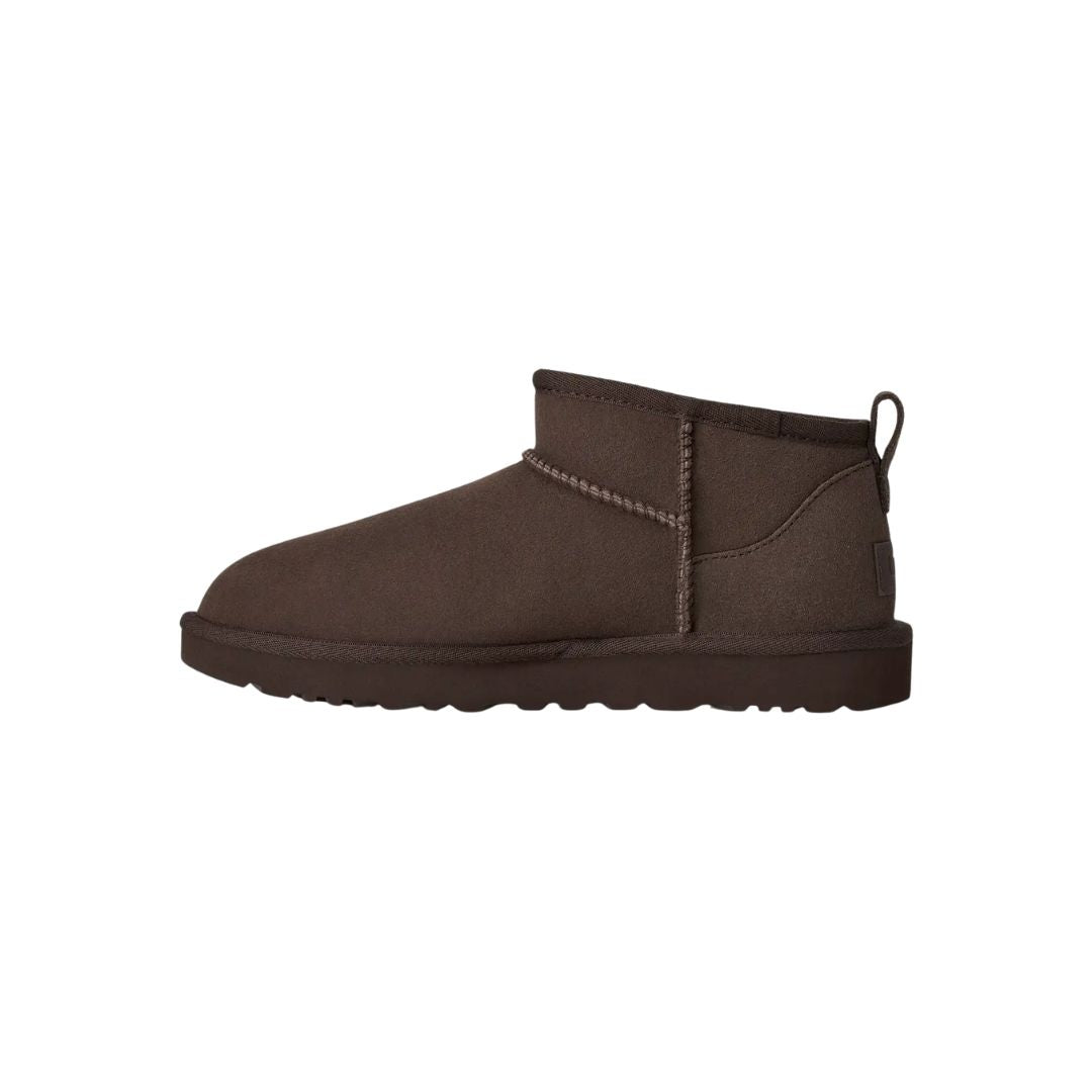 Vista lateral de la bota UGG Classic Ultra Mini en color dusted cocoa mostrando la línea superior asimétrica, el pespunte central decorativo y la caña ultra corta.