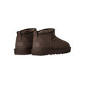 Par de botas UGG Classic Ultra Mini en color dusted cocoa vistas desde atrás en ángulo, mostrando la trabilla trasera, el contrafuerte y la suela flexible de goma.