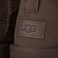 Primer plano del talón de la bota UGG Classic Ultra Mini en color dusted cocoa con la etiqueta de piel grabada con el logotipo UGG y las costuras decorativas.