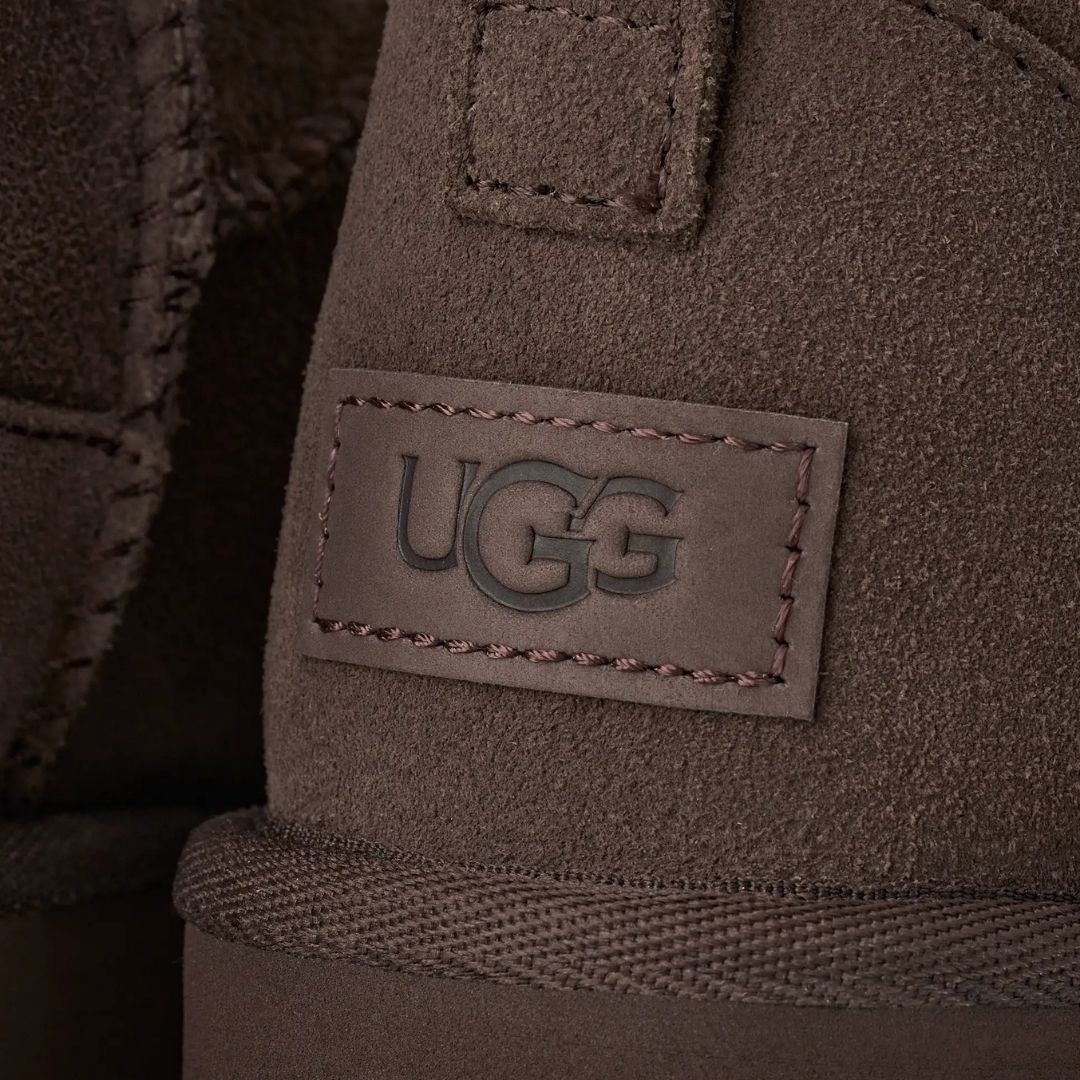 Primer plano del talón de la bota UGG Classic Ultra Mini en color dusted cocoa con la etiqueta de piel grabada con el logotipo UGG y las costuras decorativas.