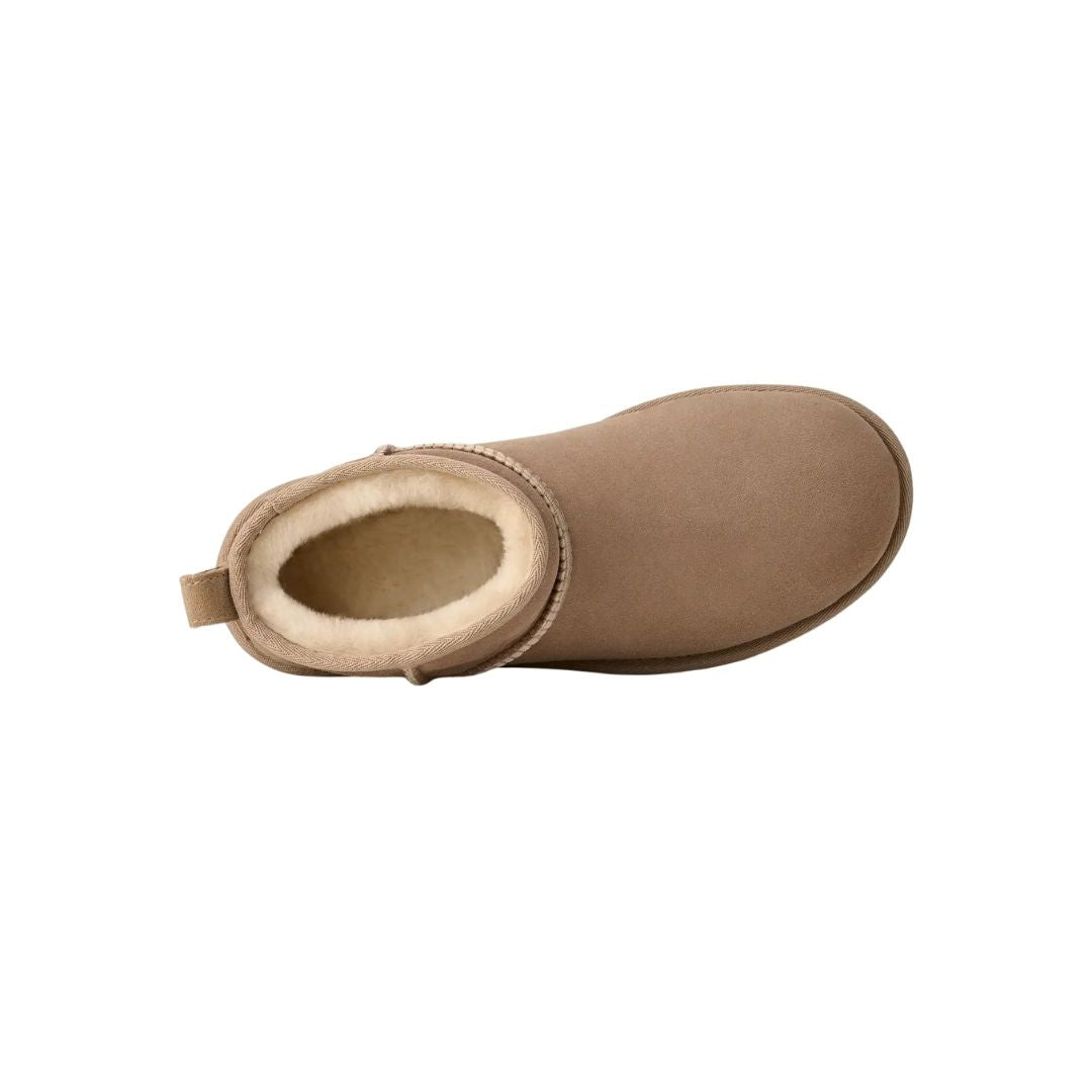Vista cenital de la bota UGG Classic Ultra Mini en color sand mostrando el interior forrado de piel de oveja en tono crudo y la trabilla trasera para calzarla fácil.