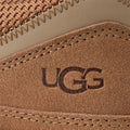 Primer plano del talón de la zapatilla UGG Lowmel en color chestnut, con el logotipo UGG grabado sobre el ante y el tejido de malla técnica de la parte trasera.