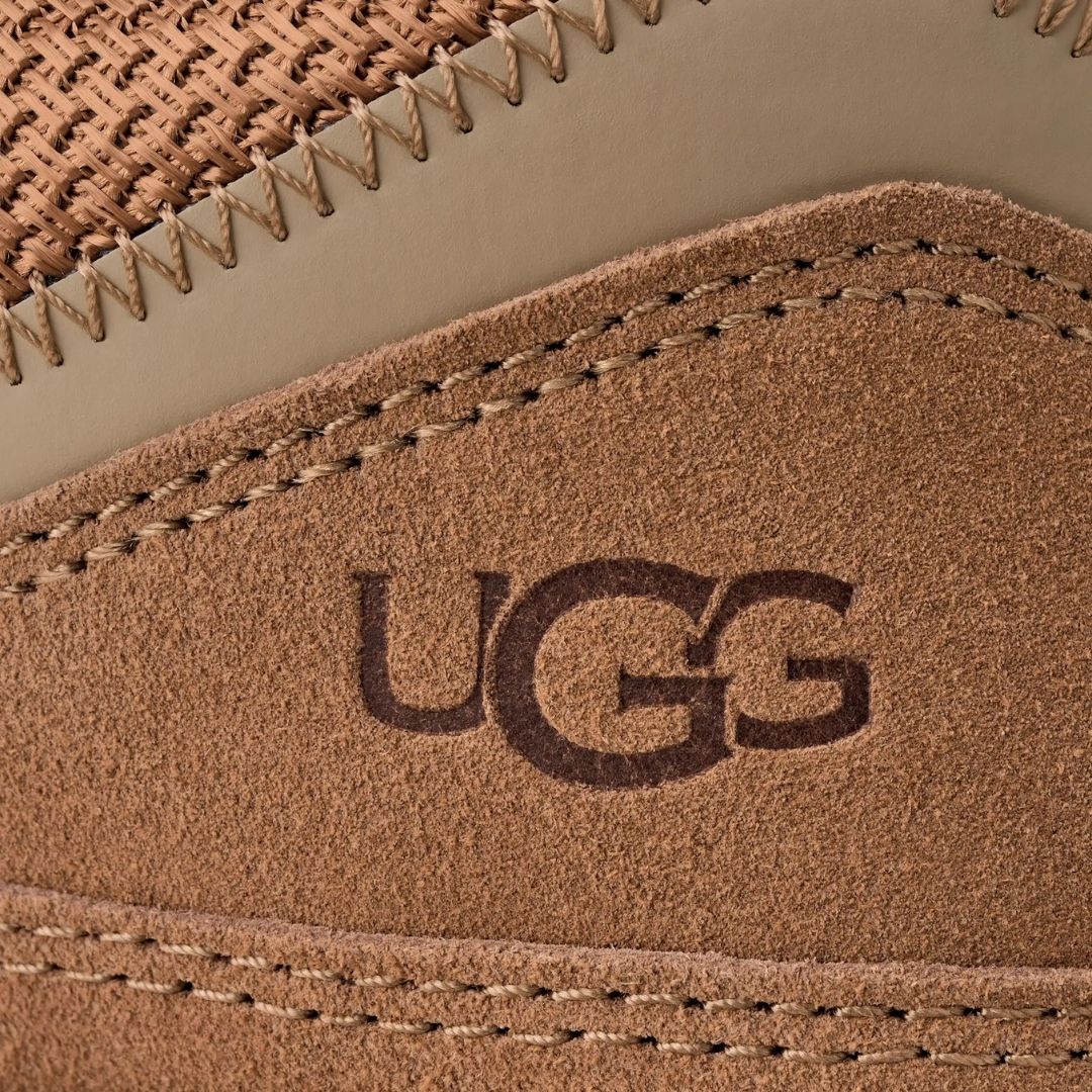 Primer plano del talón de la zapatilla UGG Lowmel en color chestnut, con el logotipo UGG grabado sobre el ante y el tejido de malla técnica de la parte trasera.