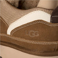 Primer plano del lateral de la zapatilla UGG Lowmel en color light bronze con el logotipo UGG grabado en ante y la combinación de malla técnica y textil crudo.