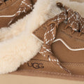 Primer plano del empeine de la zapatilla UGG Lowmel Mule en color chestnut, con los cordones bicolor anudados y el logotipo UGG grabado en el lateral del talón.