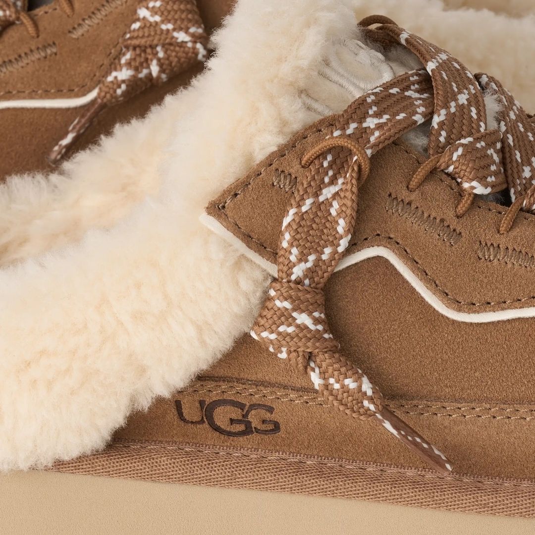 Primer plano del empeine de la zapatilla UGG Lowmel Mule en color chestnut, con los cordones bicolor anudados y el logotipo UGG grabado en el lateral del talón.