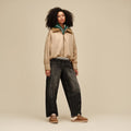 Mujer con zapatillas UGG Lowmel Mule en color chestnut combinadas con vaqueros anchos negros y chaqueta beige, mostrando el forro de piel de oveja visible en el talón.