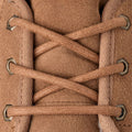 Primer plano de los cordones de algodón cruzados en los ojetes metálicos de la bota chukka UGG Neumel en color chestnut sobre el empeine de ante suave.
