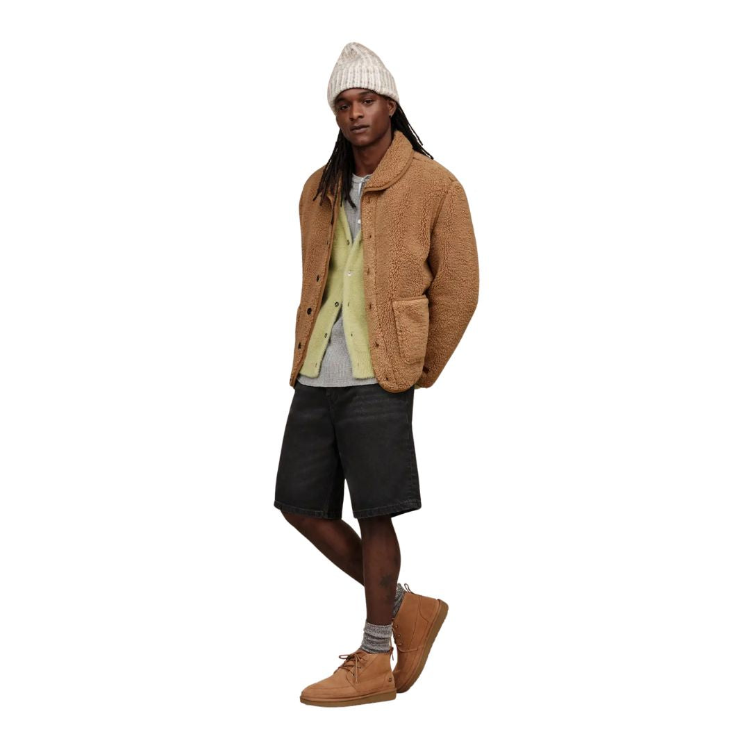 Modelo vistiendo botas UGG Neumel Moc color castaño combinadas con pantalón corto negro y chaqueta marrón.