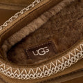 Primer plano del interior del zueco UGG Tazz II en color light bronze con la etiqueta UGG cosida sobre la piel de oveja y el bordado geométrico del ribete.