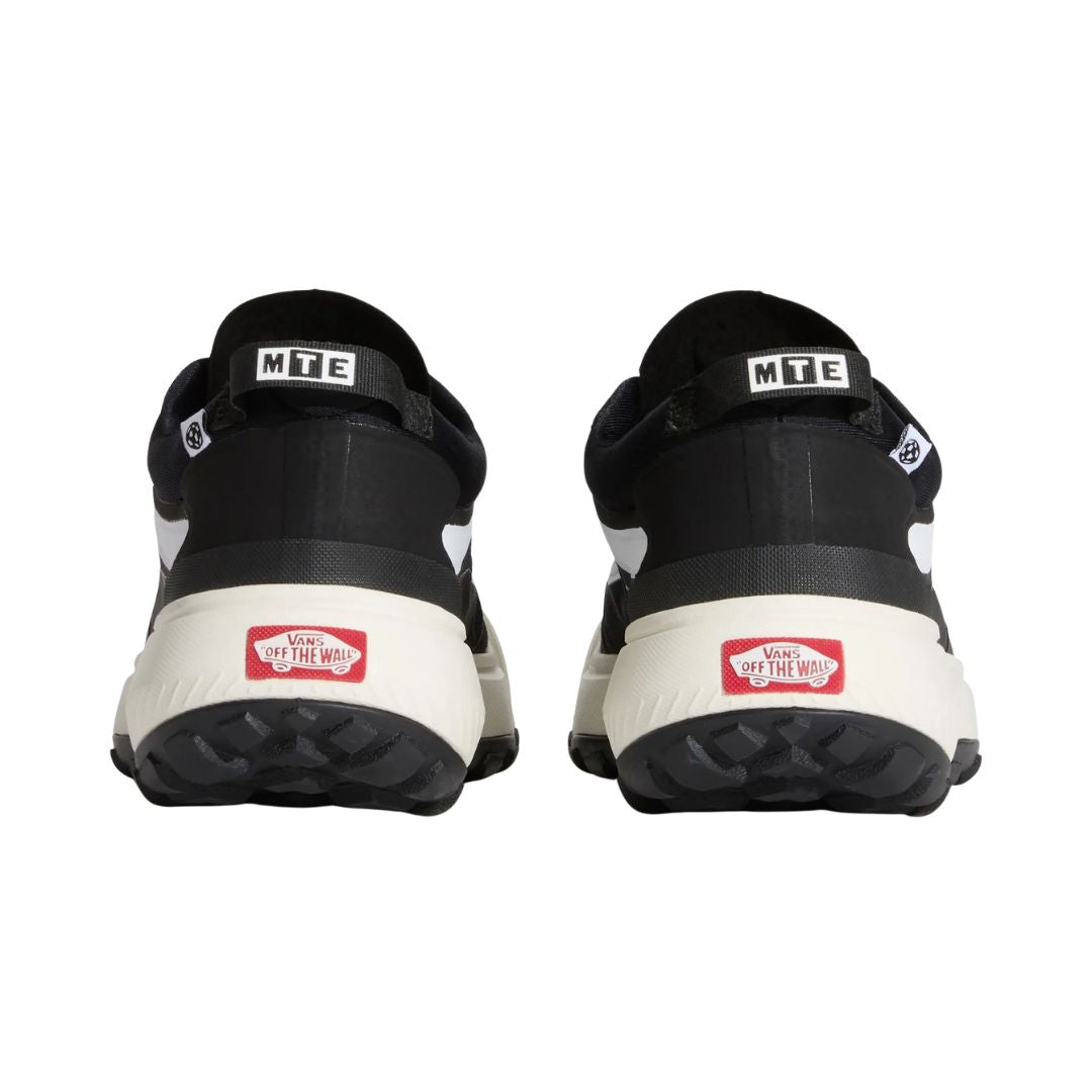 Vista trasera de un par de zapatillas Vans MTE Crosspath en negro y blanco, con los tiradores de talón MTE y los parches rojos Vans Off The Wall sobre la suela clara.