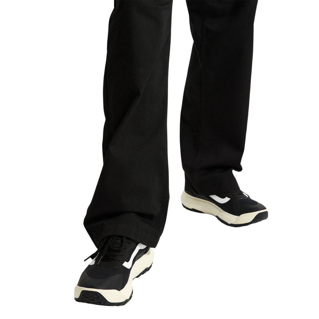 Detalle de las piernas de un hombre con pantalón ancho negro calzando las zapatillas Vans MTE Crosspath en negro y blanco, vista frontal de ambos pies caminando.