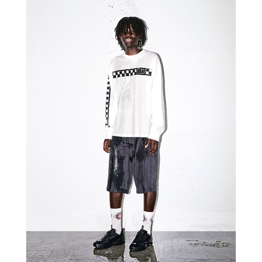 Hombre con camiseta Vans blanca de manga larga y logo a cuadros, pantalón corto oscuro y calcetines Vans, calzando las zapatillas Vans Crosspath XC Gore-Tex en negro bajo un efecto de agua salpicando.